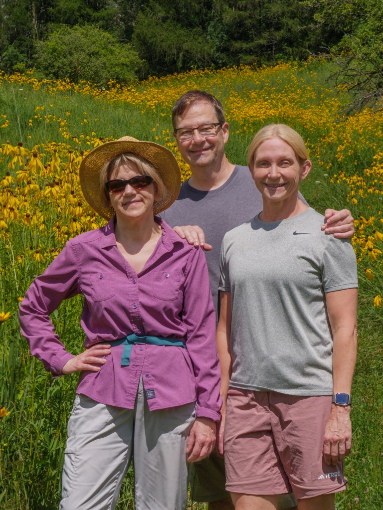 Two lovely women and a fine gentleman in a field of flowers on a sunny day.